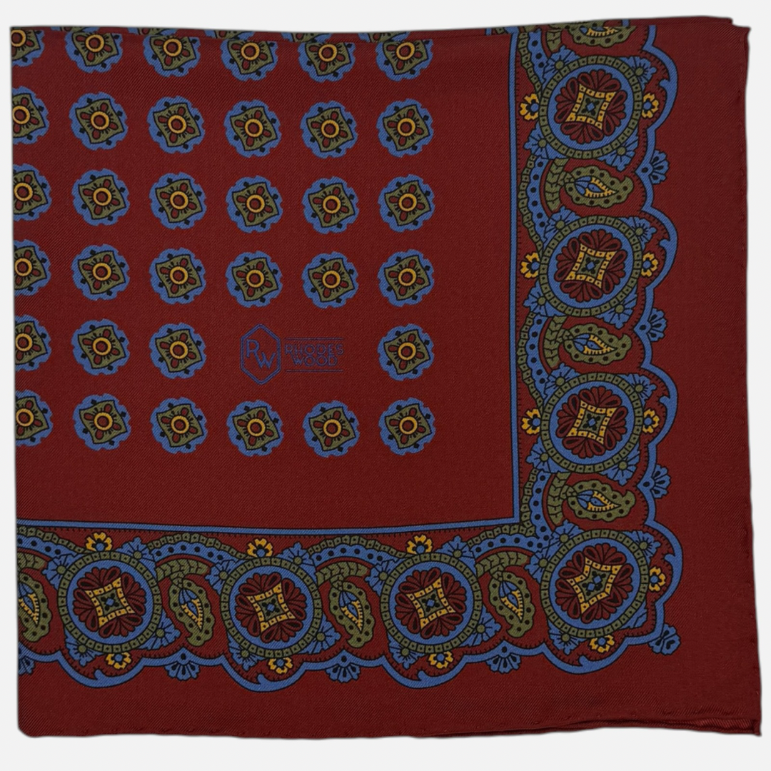 A deep red pocket square with green and blue quatrefoils repeating across the silk.