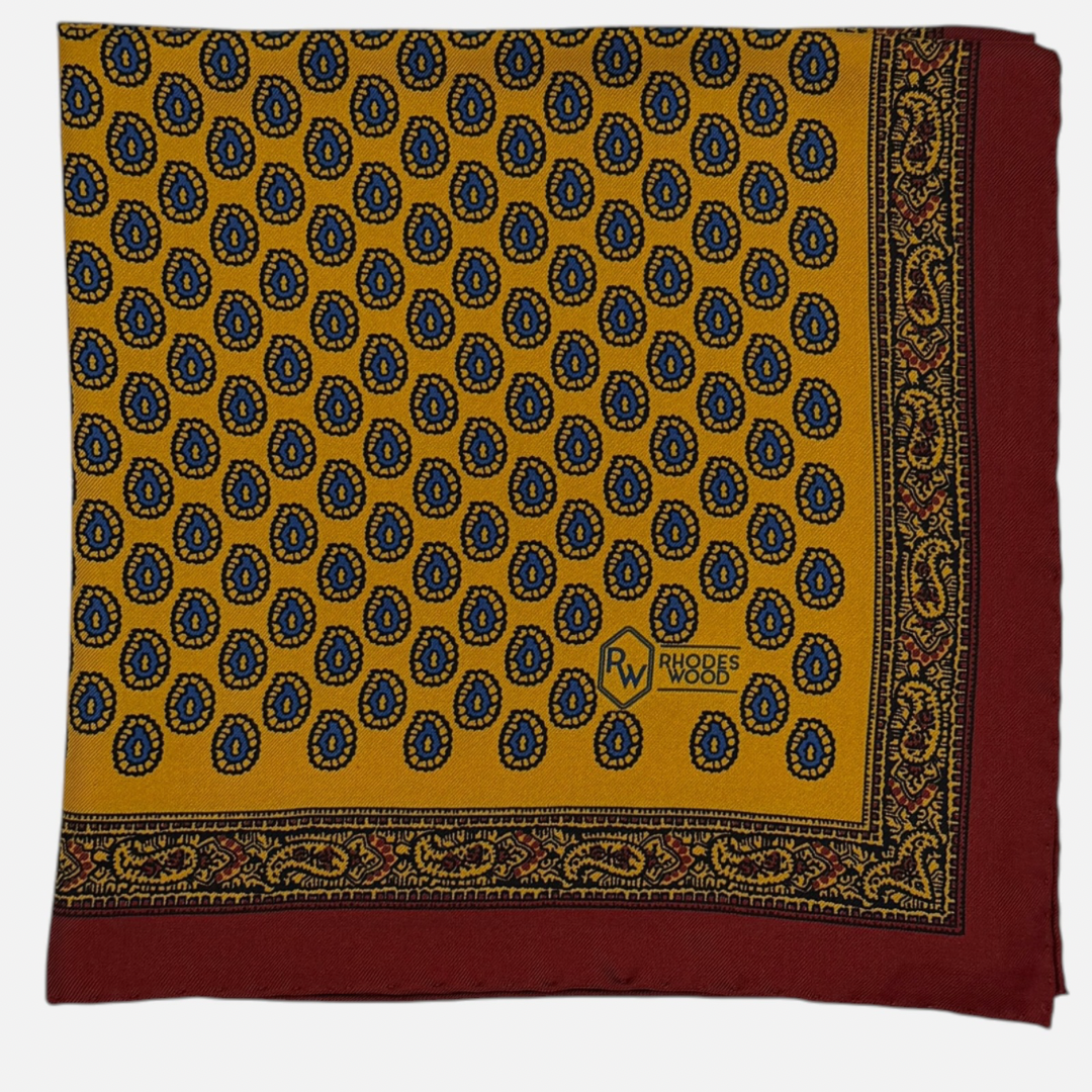 Yellow pocket square with a red border and blue teardrop paisley repeating across the silk.
