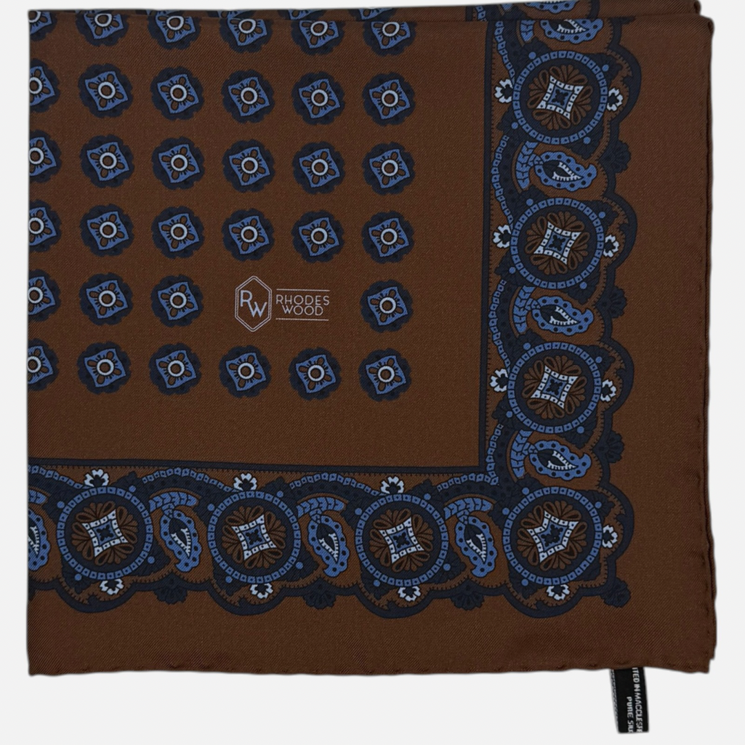 Brown pocket square with light blue & navy quatrefoils repeating across the silk. 