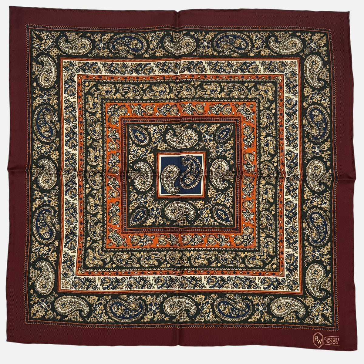 A burgundy border pocket quare with large repeating paisley design across the silk. 
