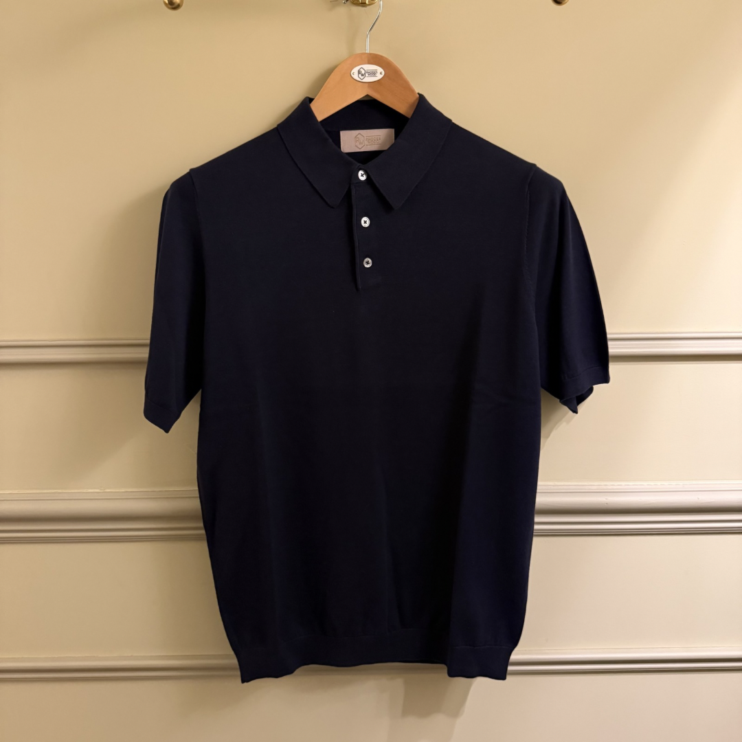 Navy blue polo shirt on a hanger against a beige wall.