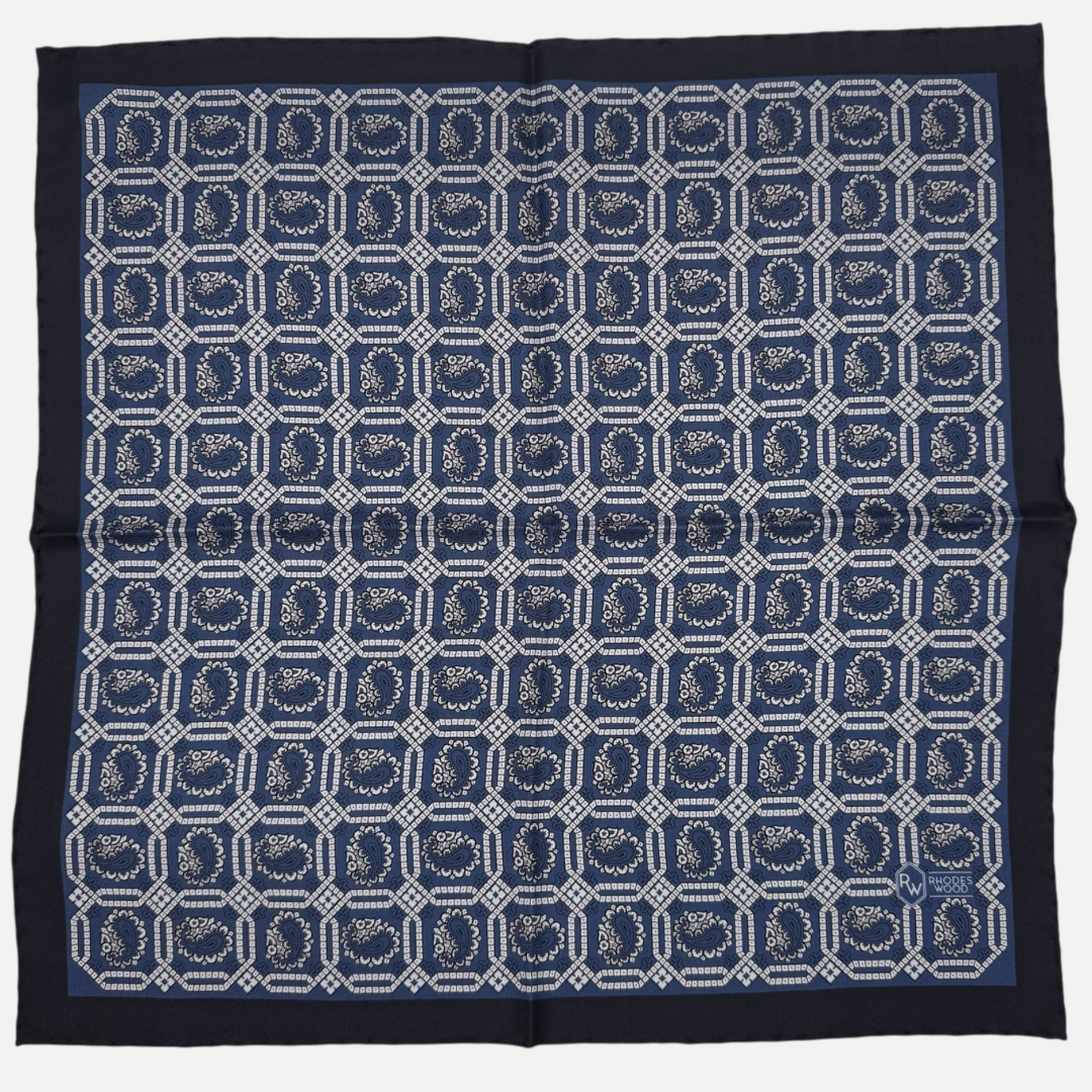 A navy blue pocket square with sky blue octagon paisleys repeating across the silk.