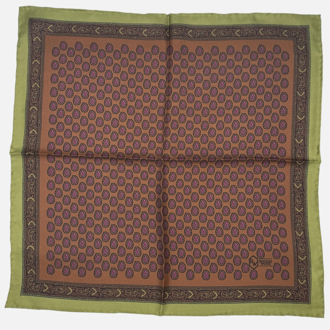 A brown pocket square with an olive green border. Featuring purple rear drop paisleys repeating across the silk.