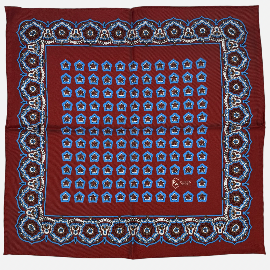 An oxblood and blue star medallion pocket square. The star medallions are oxblood and blue repeating across the oxblood colour silk. 