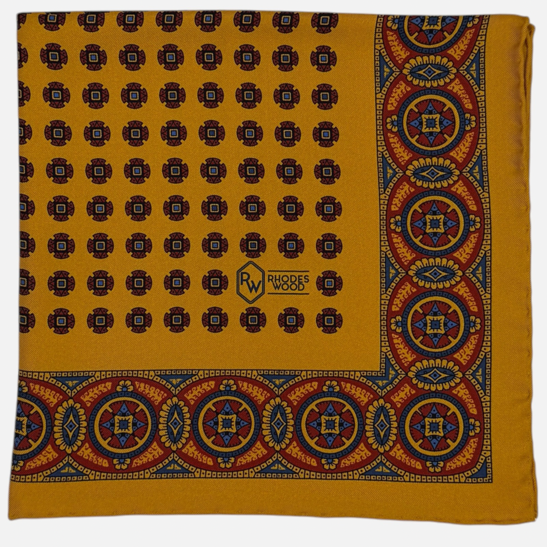 A gold pocket square with rich deep red and blue medallions repeating across the silk. 