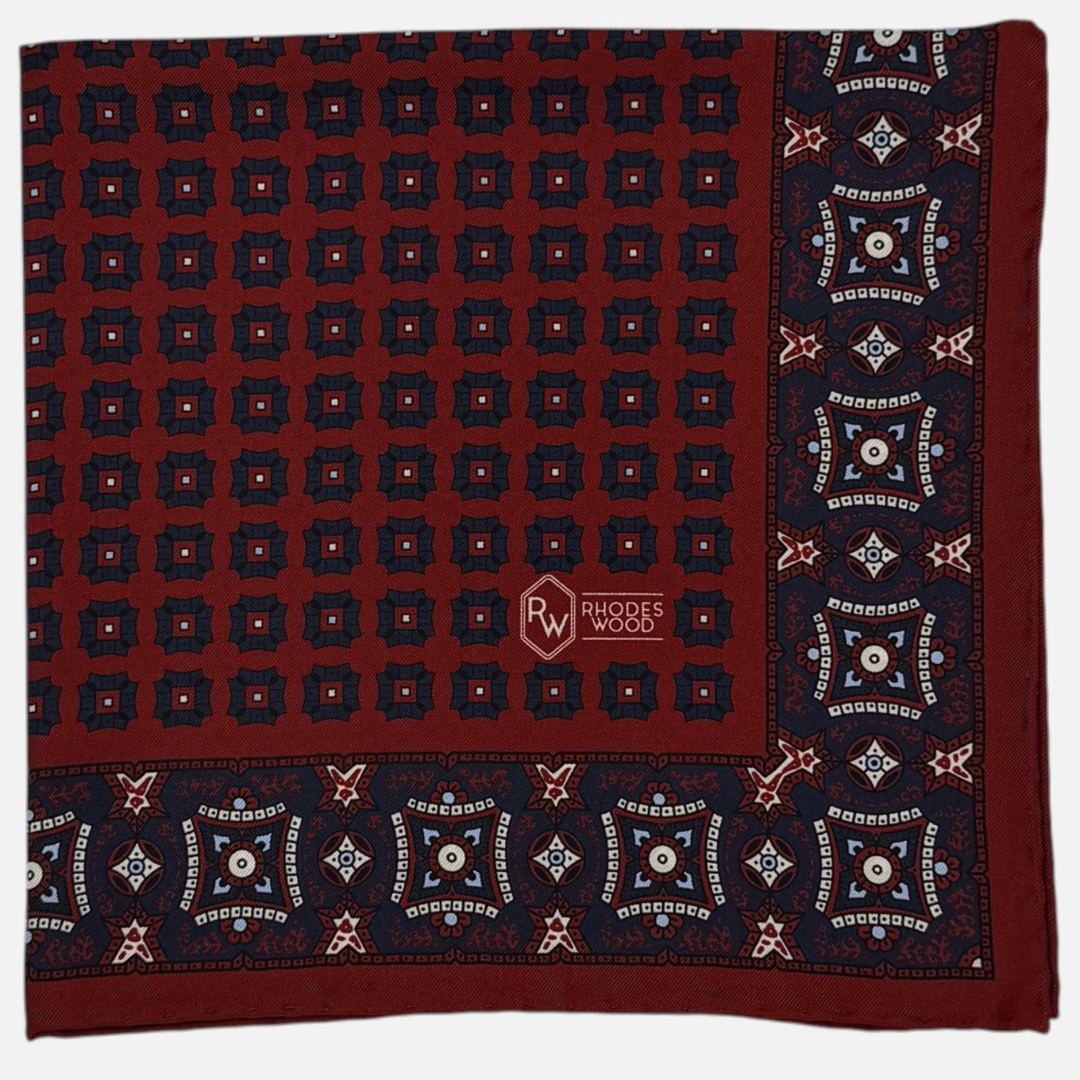 Claret pocket square with navy blue mosaics repeating across the silk. 