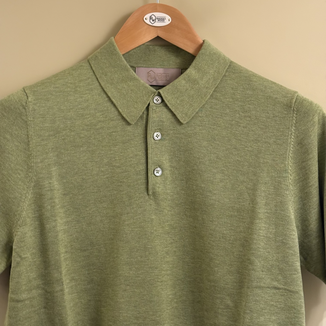 Green polo shirt on a hanger against a beige background