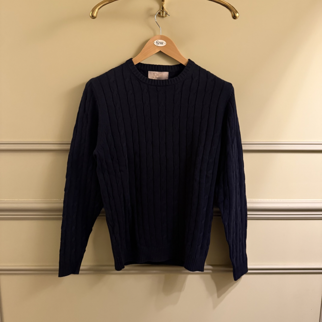 Navy blue sweater on a hanger against a beige wall.