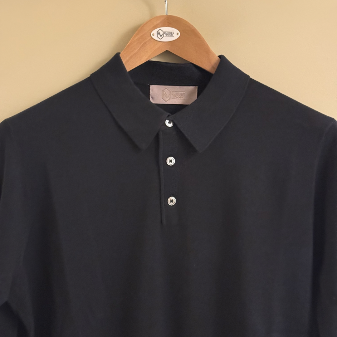 Black polo shirt on a wooden hanger against a beige background