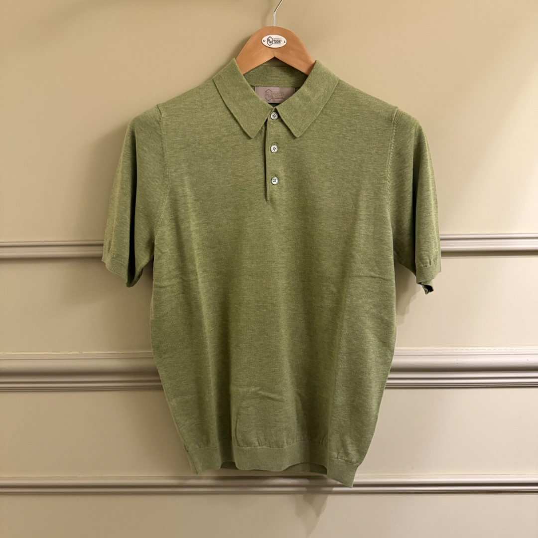 Green polo shirt on a hanger against a beige wall