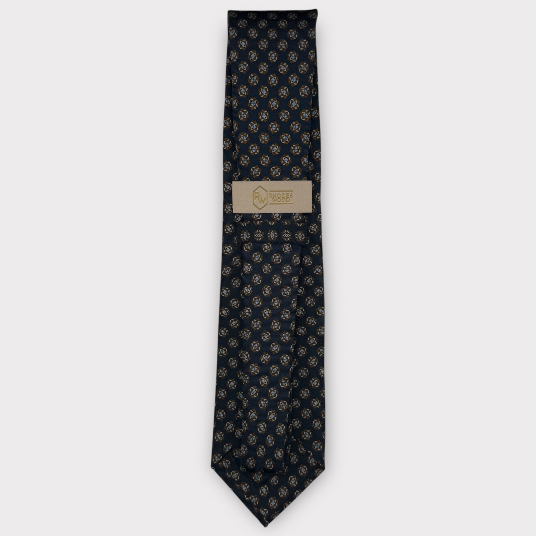 A dark navy blue necktie with a repeating gold anchor pattern, featuring a beige paper brand label in the center.