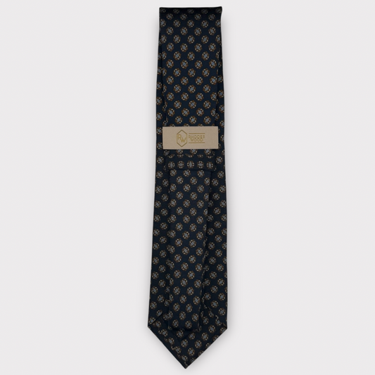 A dark navy blue necktie with a repeating gold anchor pattern, featuring a beige paper brand label in the center.