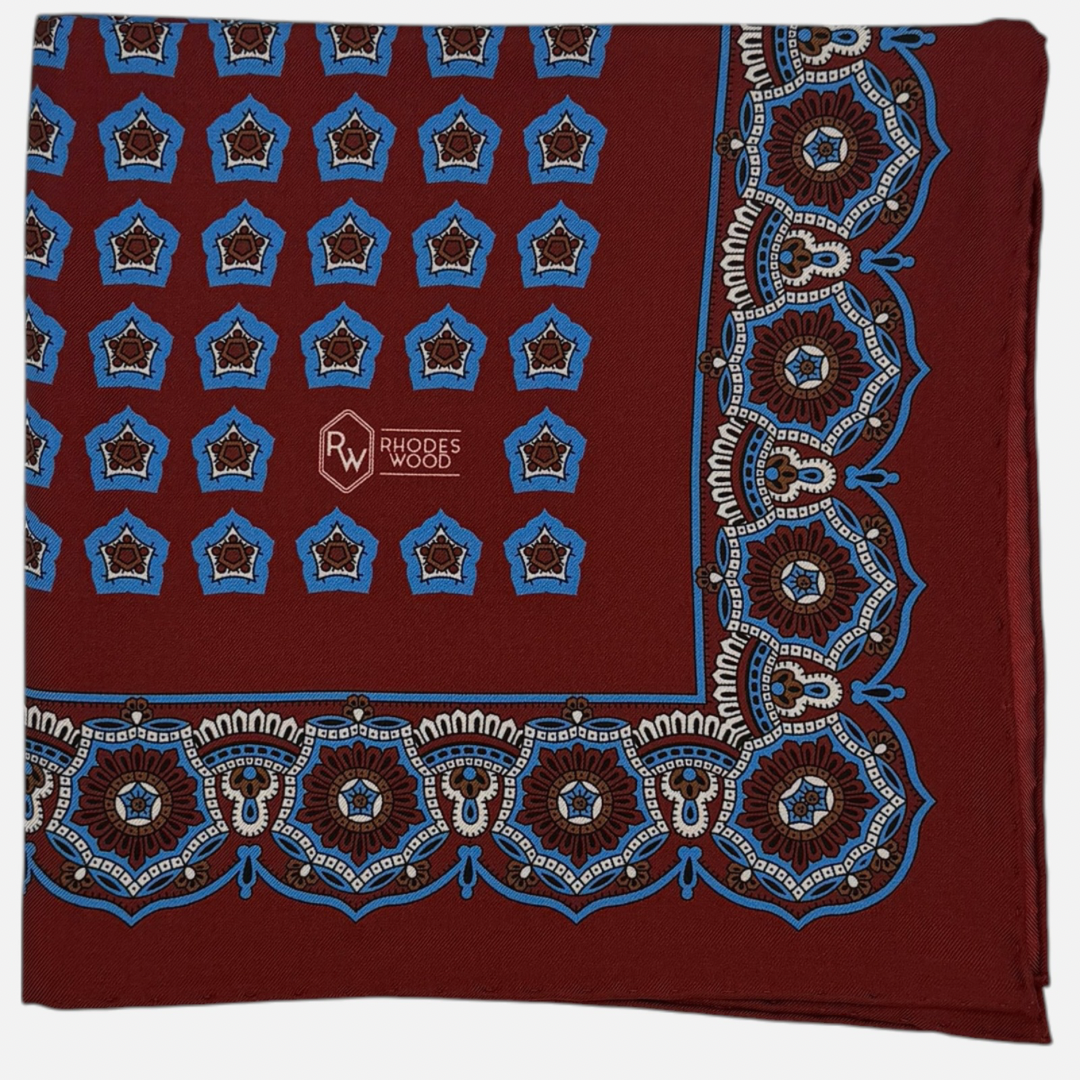 An oxblood and blue star medallion pocket square. The star medallions are oxblood and blue repeating across the oxblood colour silk. 