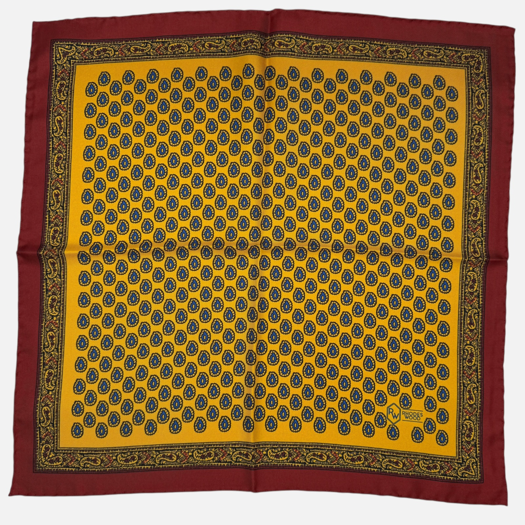 Yellow pocket square with a red border and blue teardrop paisley repeating across the silk.