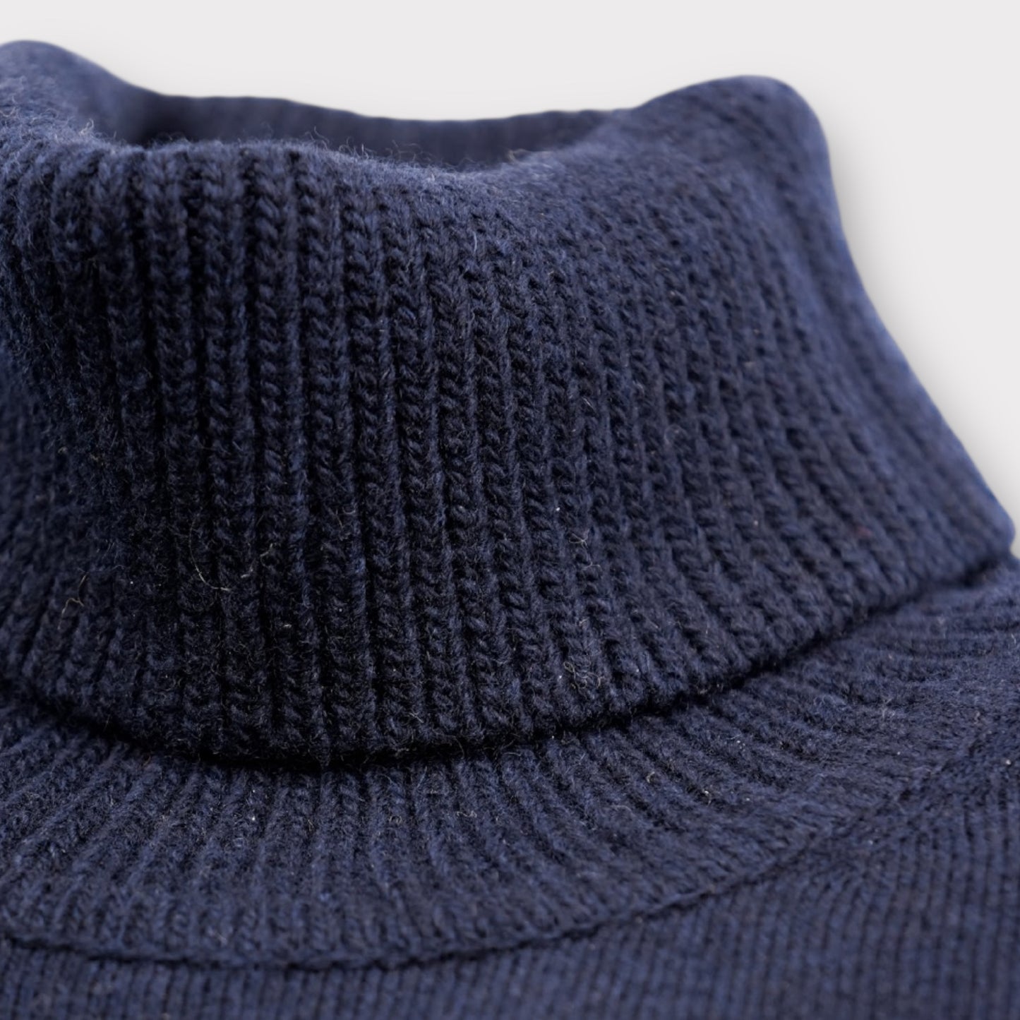 Close-up of a navy blue knitted sweater with a high collar on a light gray background