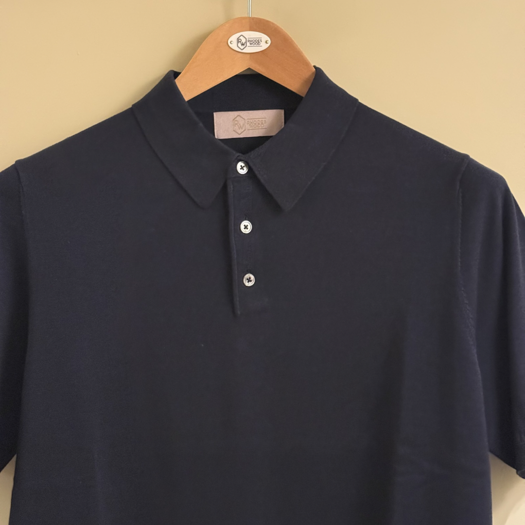 Bottle green  polo shirt on a wooden hanger against a beige background