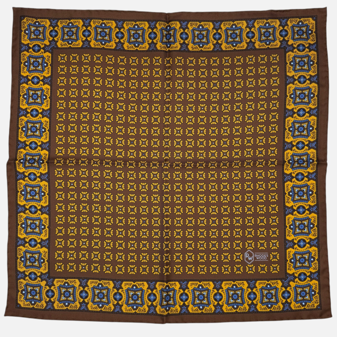 A brown pocket square with yellow mosaic pattern repeating across the silk.