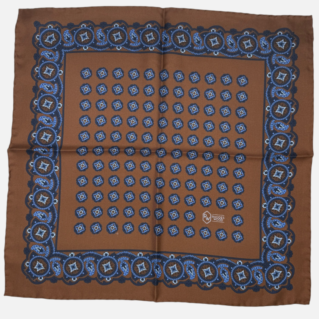 Brown pocket square with light blue & navy quatrefoils repeating across the silk. 