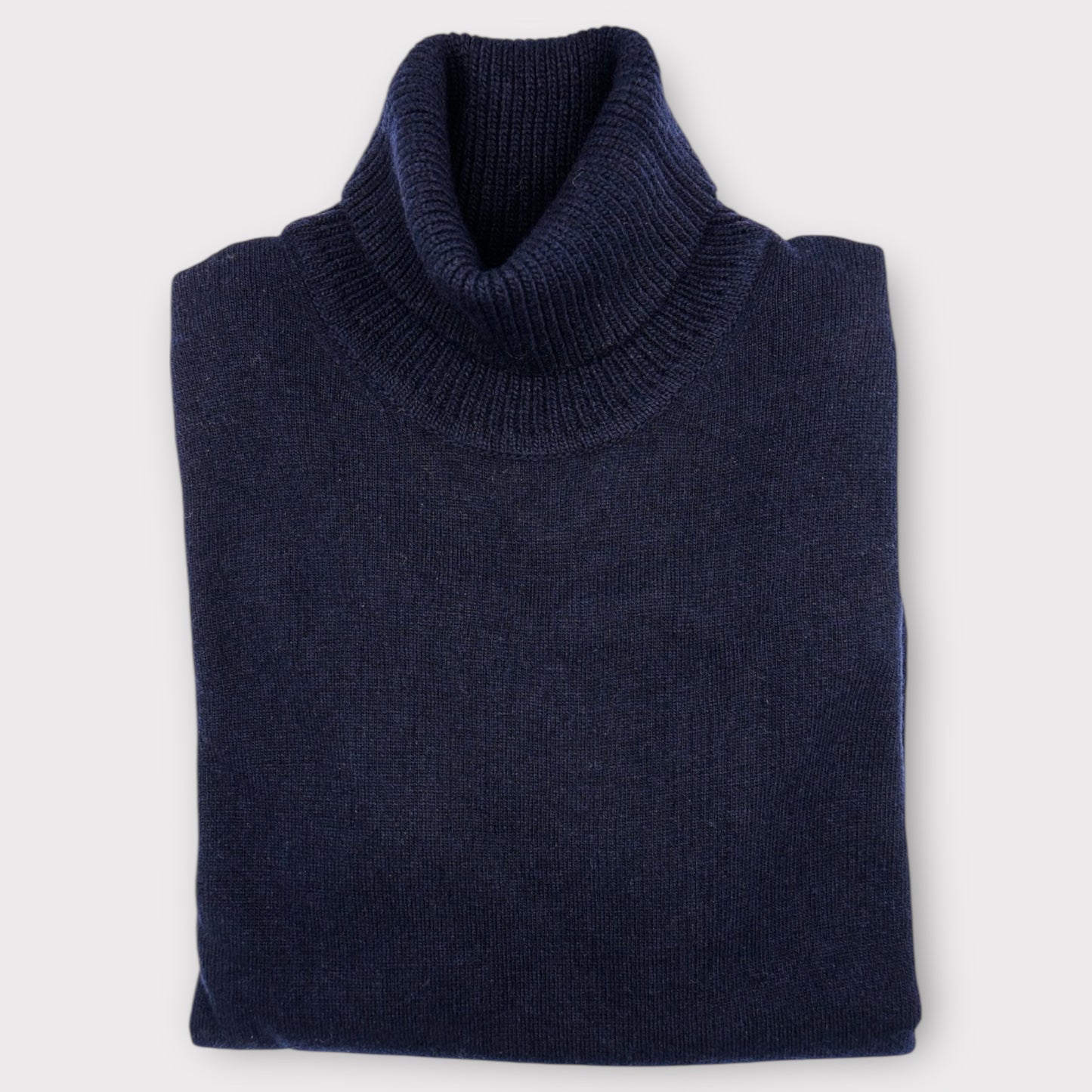 Folded navy blue Roll Neck sweater on a light gray background