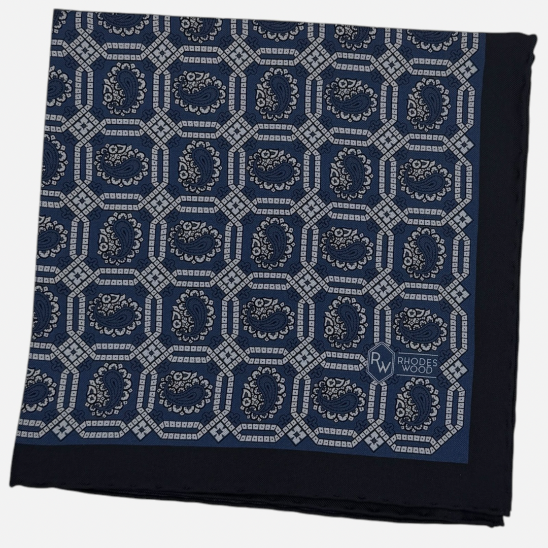 A navy blue pocket square with sky blue octagon paisleys repeating across the silk.