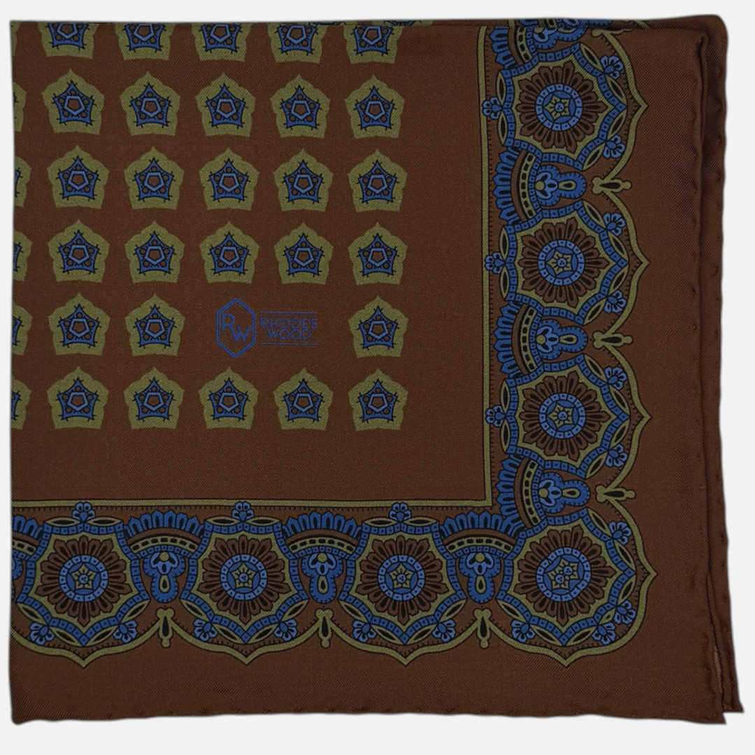 A brown silk pocket squares with light green and blue medallions repeating across the silk 