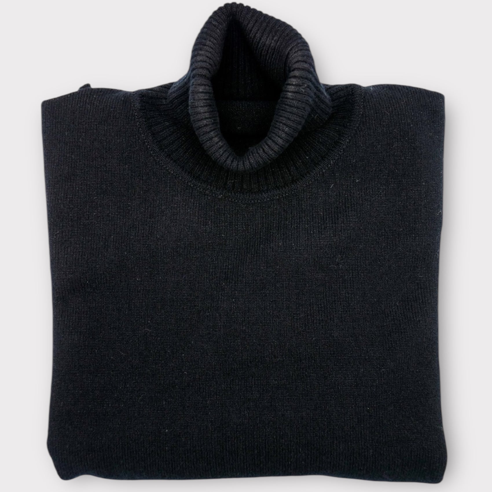 Folded navy blue Roll Neck sweater on a light gray background
