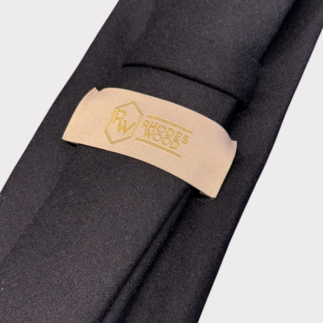 Black tie with a beige tie clip featuring a logo and text on a light gray background