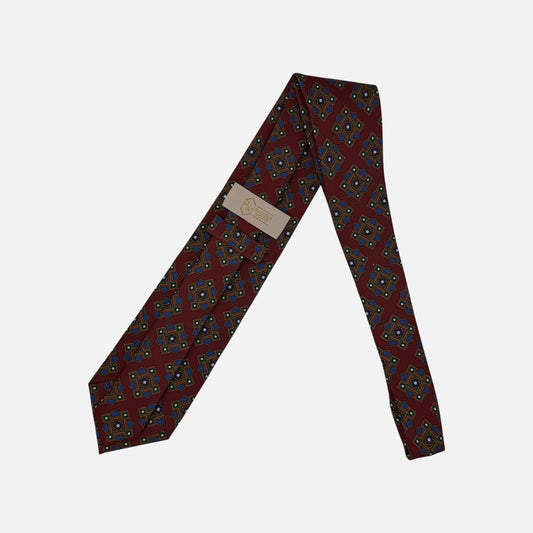 A burgundy neck tie with blue and green large medallions.