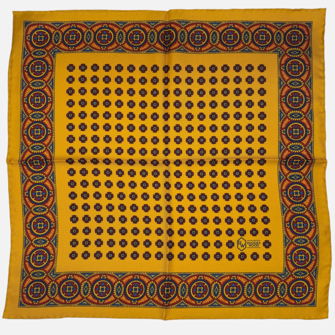 A gold pocket square with rich deep red and blue medallions repeating across the silk. 