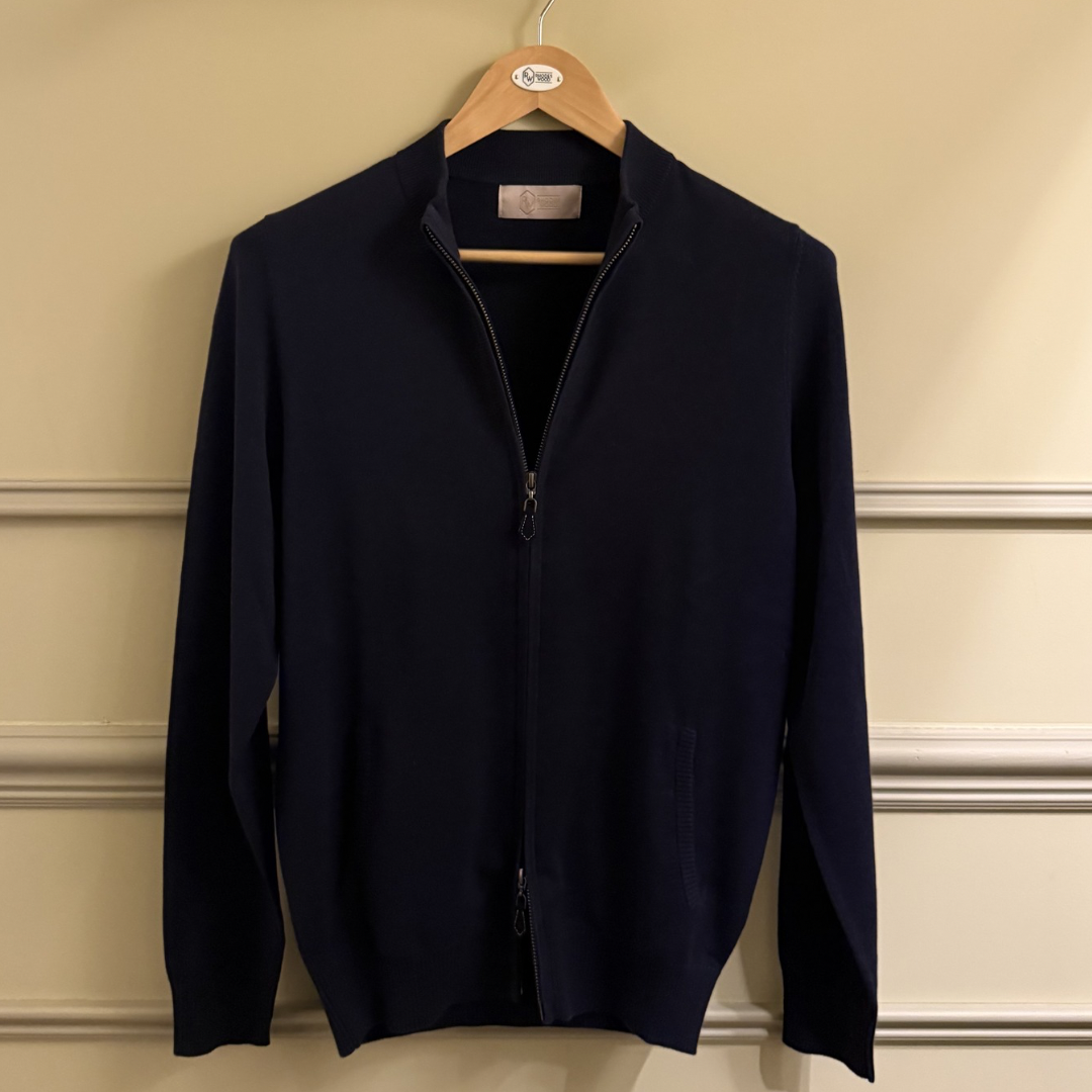 Navy blue jacket on a hanger against a beige wall.