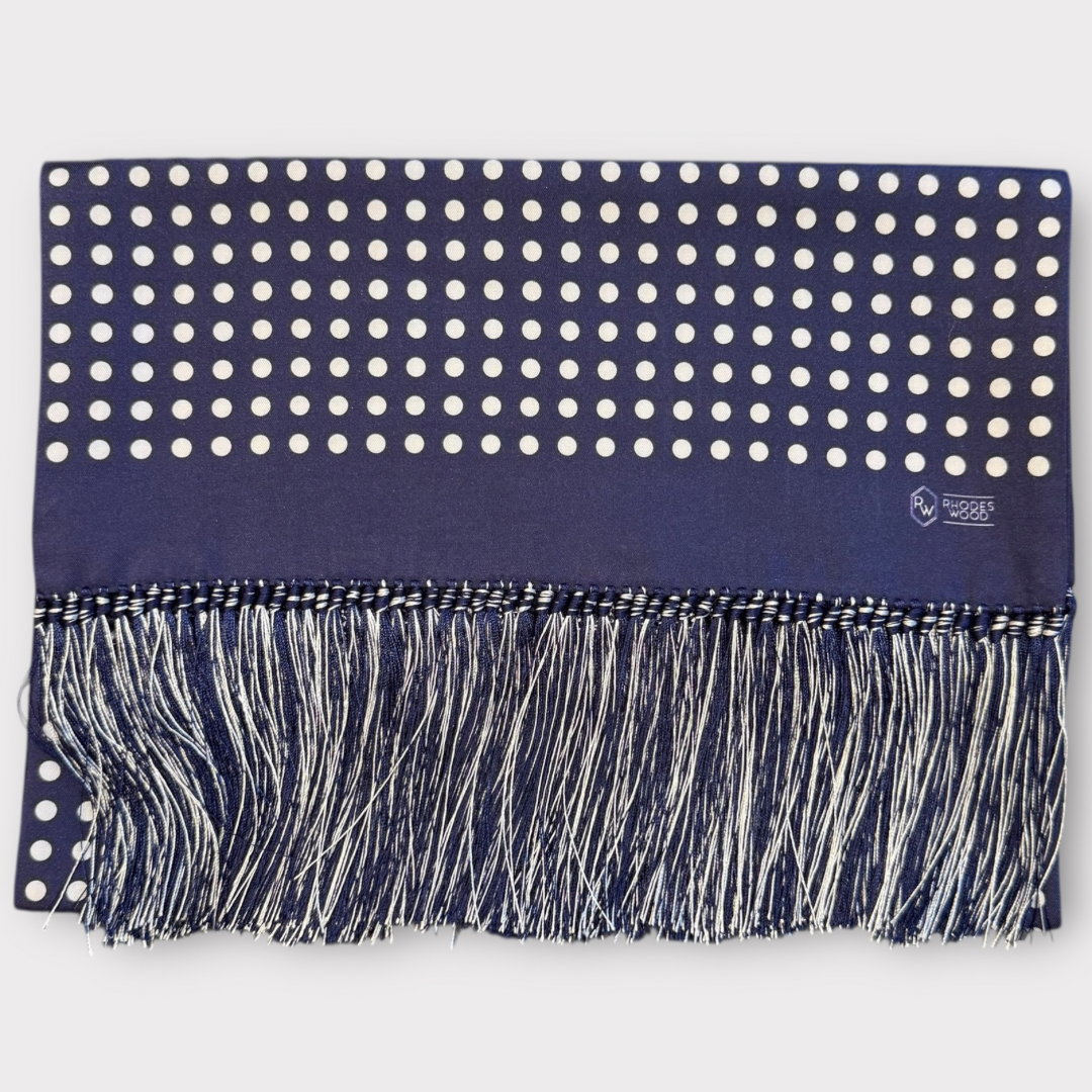 Navy blue scarf with white polka dots and fringe on a light gray background