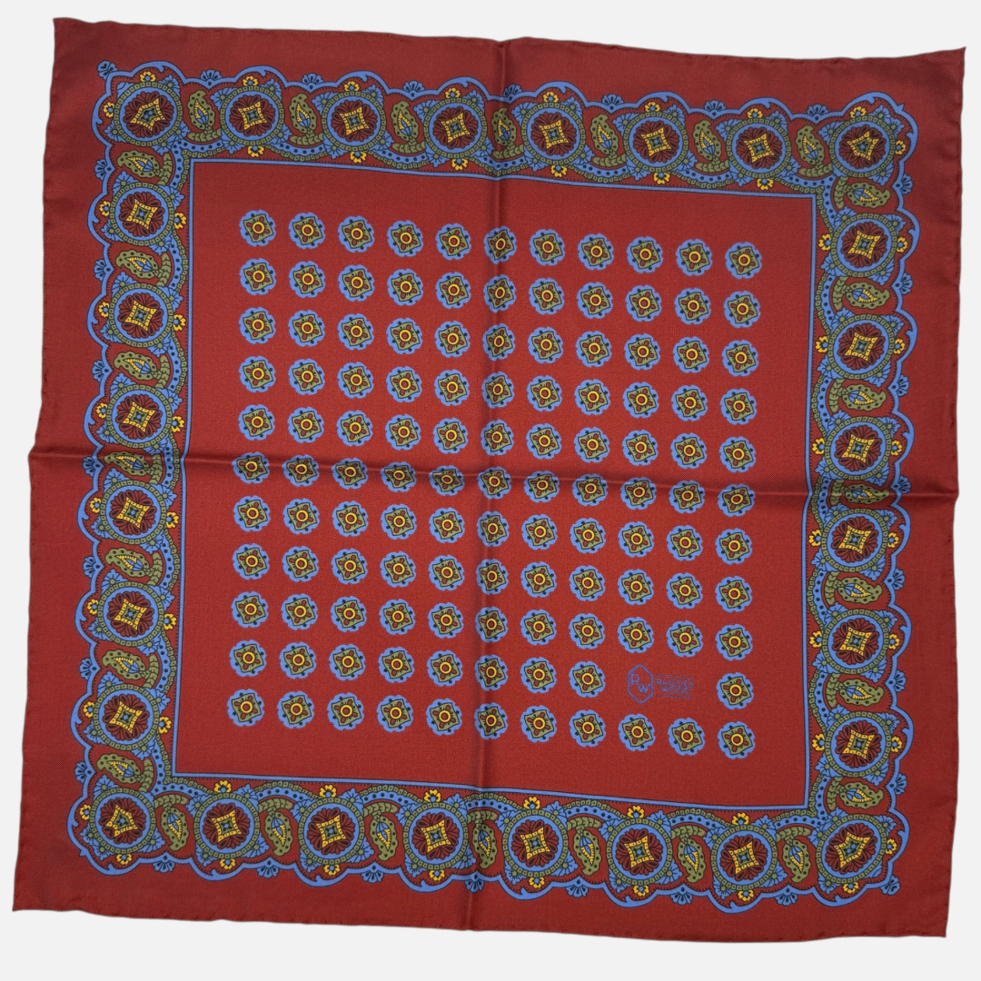 A deep red pocket square with green and blue quatrefoils repeating across the silk.